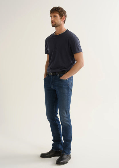 Person wearing a dark navy short sleeve t-shirt, medium indigo jeans, and black boots, angled front full body view on a light grey background.