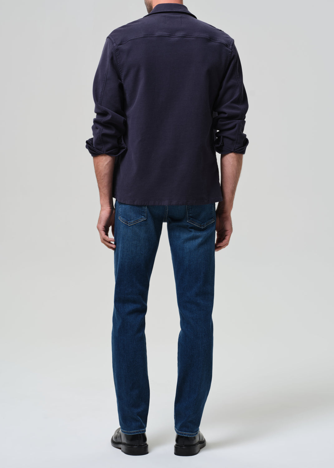Person wearing a navy shirt and blue jeans on a grey background