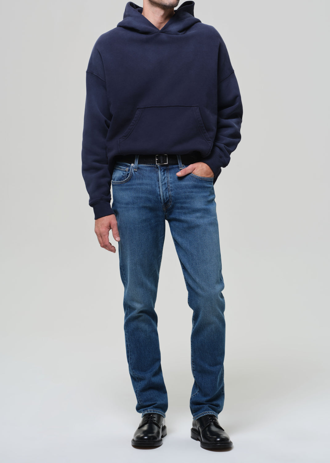 Person wearing a navy hoodie and blue jeans on a plain background