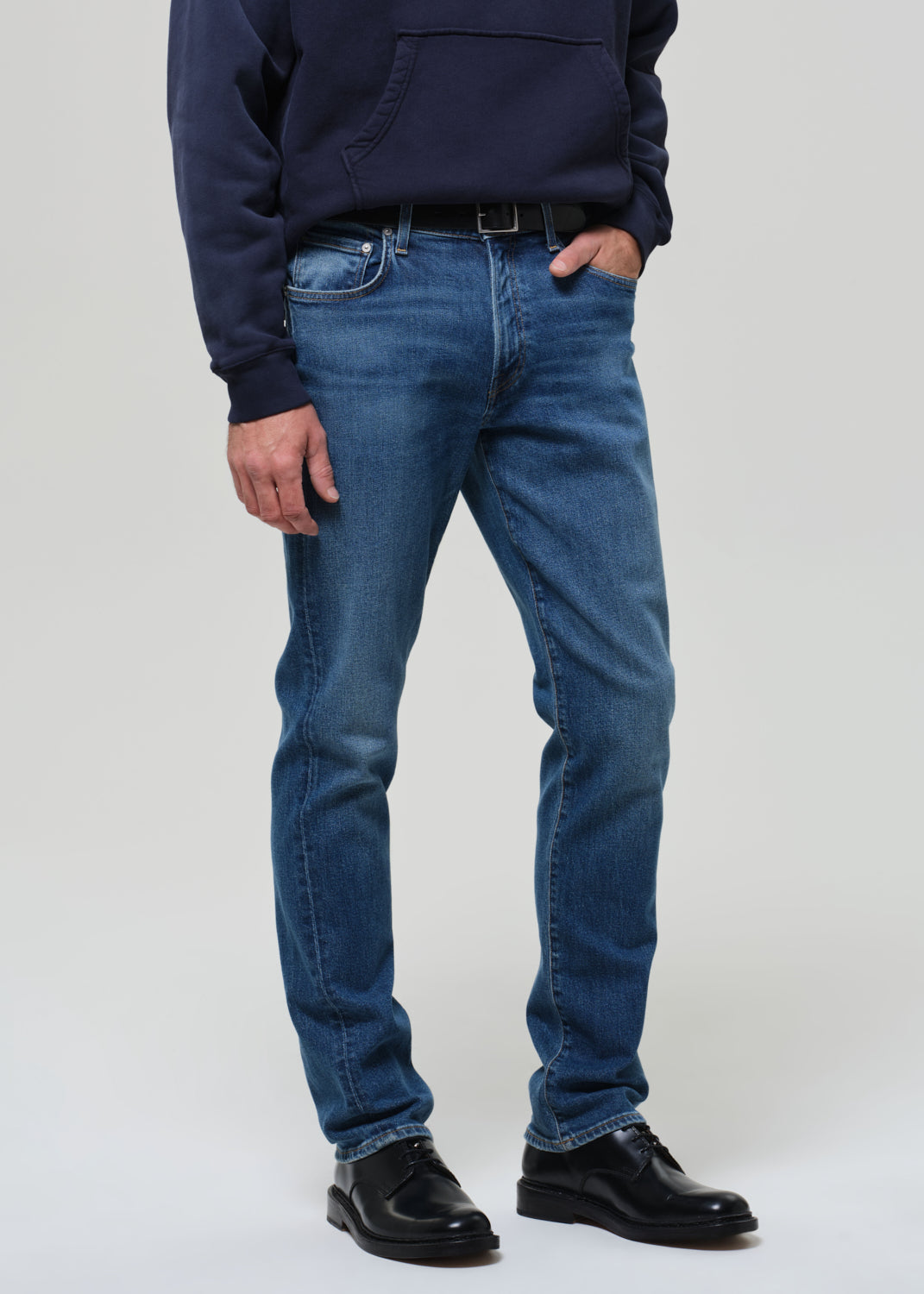 Person wearing a navy hoodie and blue jeans on a grey background