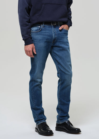 Person wearing a navy hoodie and blue jeans on a grey background