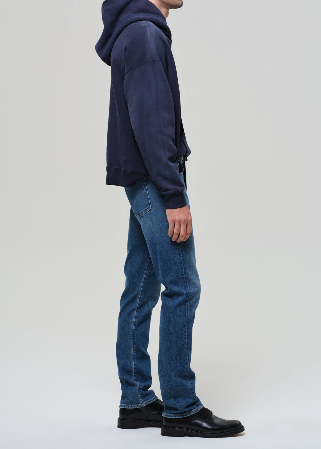 Person wearing a navy hoodie and blue jeans on a grey background