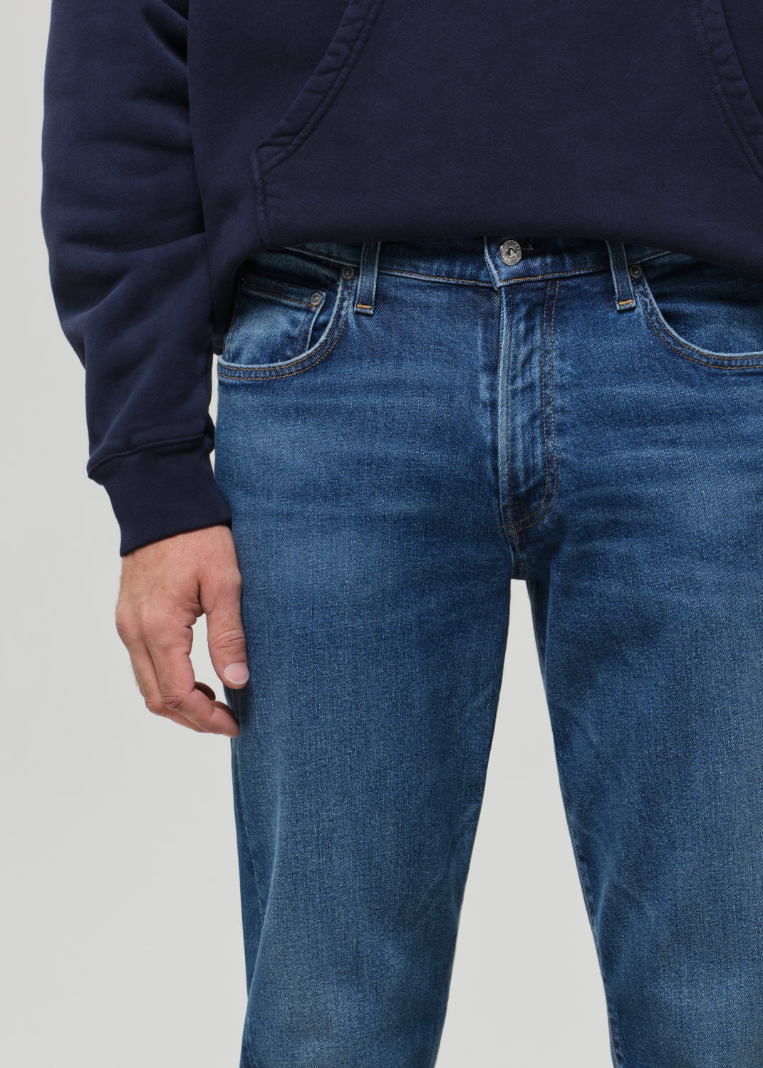 Person wearing a navy hoodie and blue jeans on a grey background