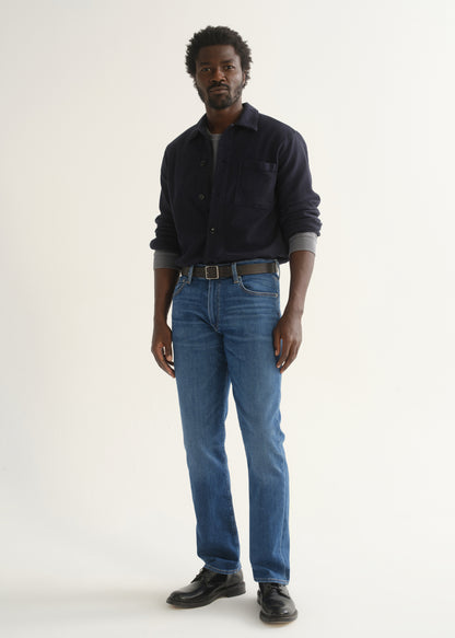 Person wearing medium blue straight leg jeans with a navy long sleeve collared pullover and black shoes, front full body view on a light grey background.
