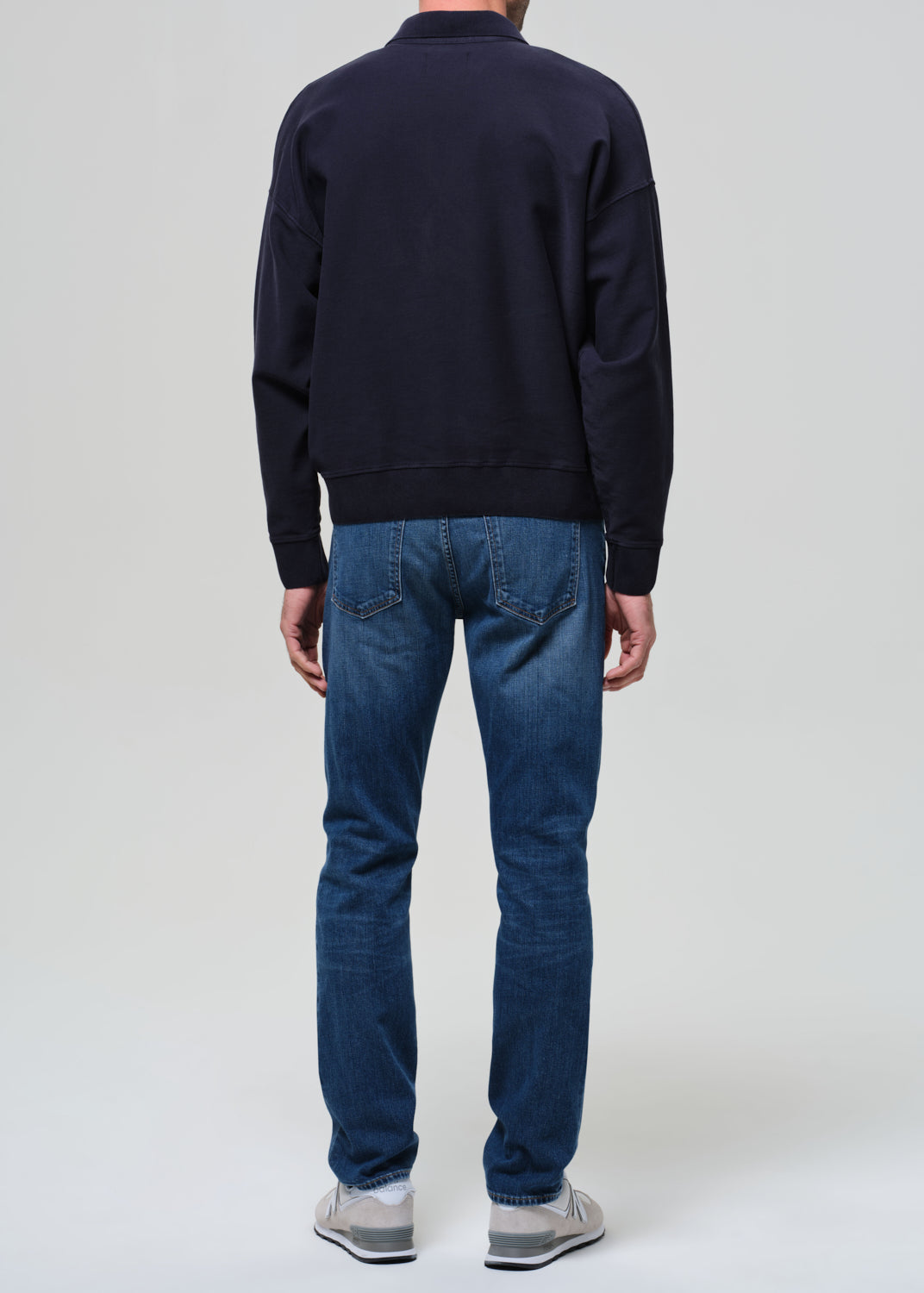 Person wearing a navy sweater and blue jeans on a white background