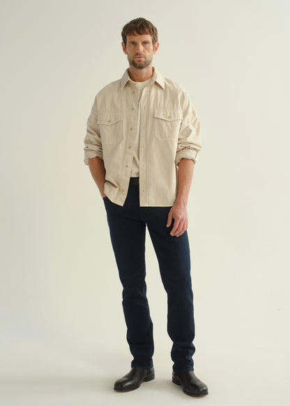 Person wearing a cream button-front shirt, dark indigo jeans, and black boots, front full body view on a light grey background.
