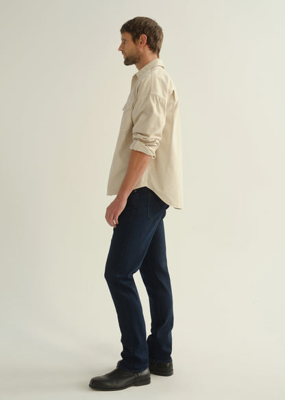 Person wearing a cream button-front shirt, dark indigo jeans, and black boots, side full body view on a light grey background.