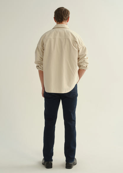 Person wearing a cream button-front shirt, dark indigo jeans, and black boots, back full body view on a light grey background.