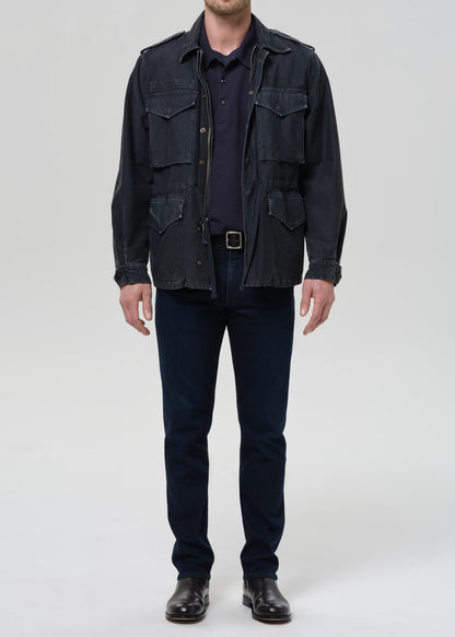 Person wearing a dark jacket, shirt, and pants on a grey background