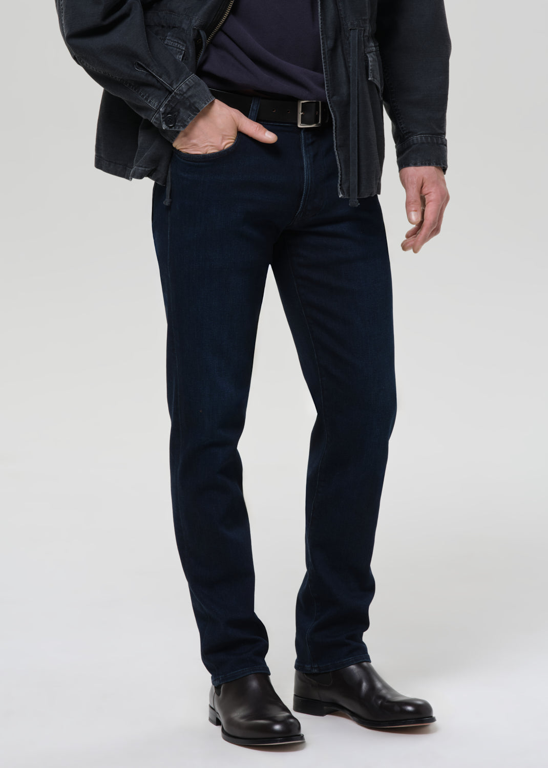 Person wearing dark blue jeans and black shoes on a grey background