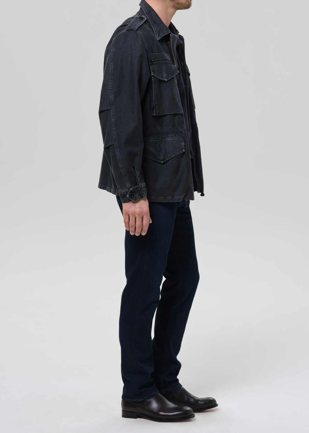 Person wearing a dark denim jacket and pants on a grey background