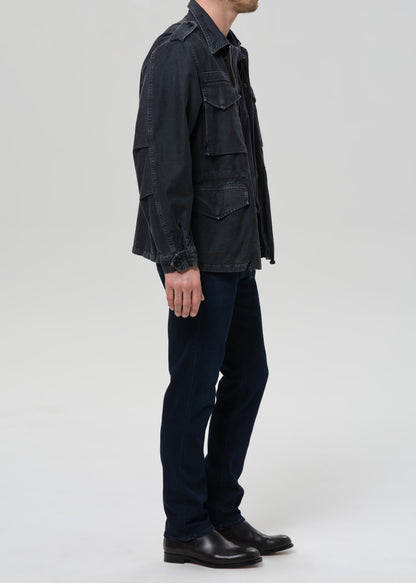 Person wearing a dark denim jacket and pants on a grey background