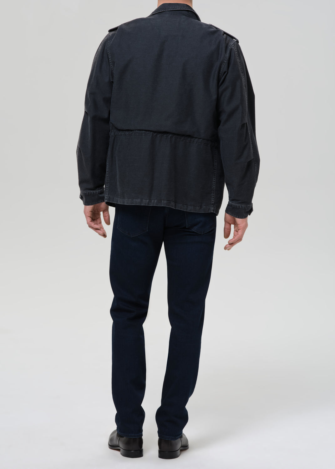 Person wearing a dark jacket and pants on a grey background