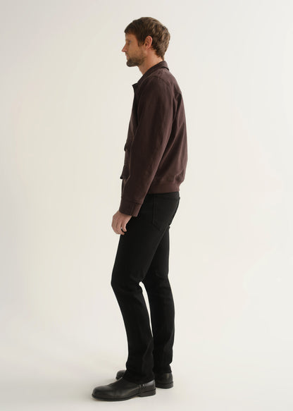 Person wearing a dark brown jacket, black pants, and black boots, side full body view on a light grey background.