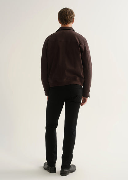 Person wearing a dark brown jacket, black pants, and black boots, back full body view on a light grey background.
