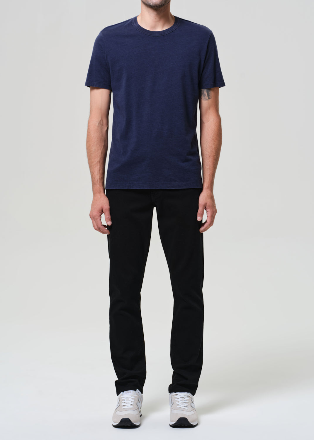 Person wearing a navy blue t-shirt and black jeans on a grey background