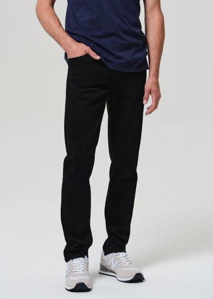 Person wearing a navy blue t-shirt and black jeans on a grey background