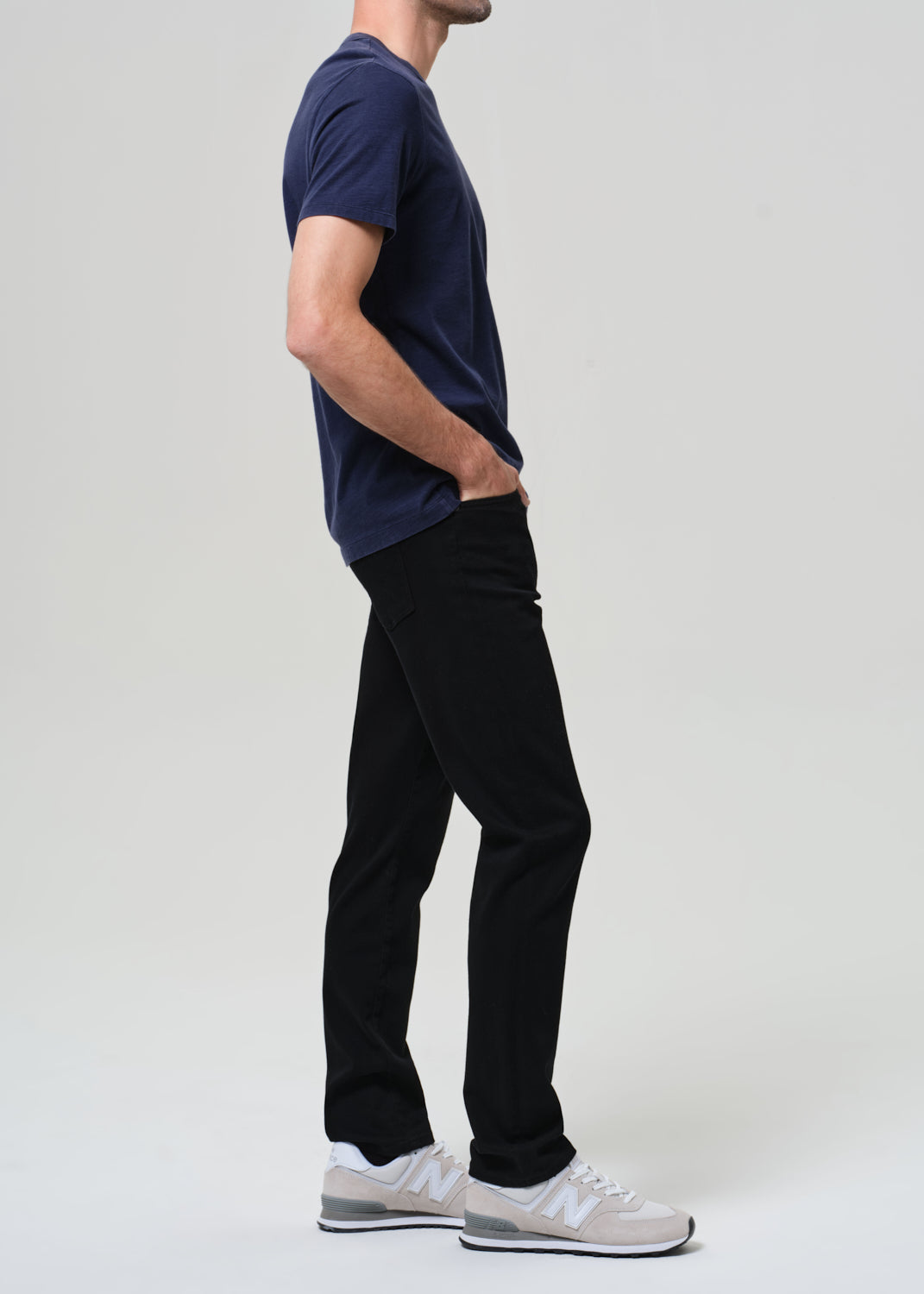 Person wearing a navy blue t-shirt and black jeans on a grey background