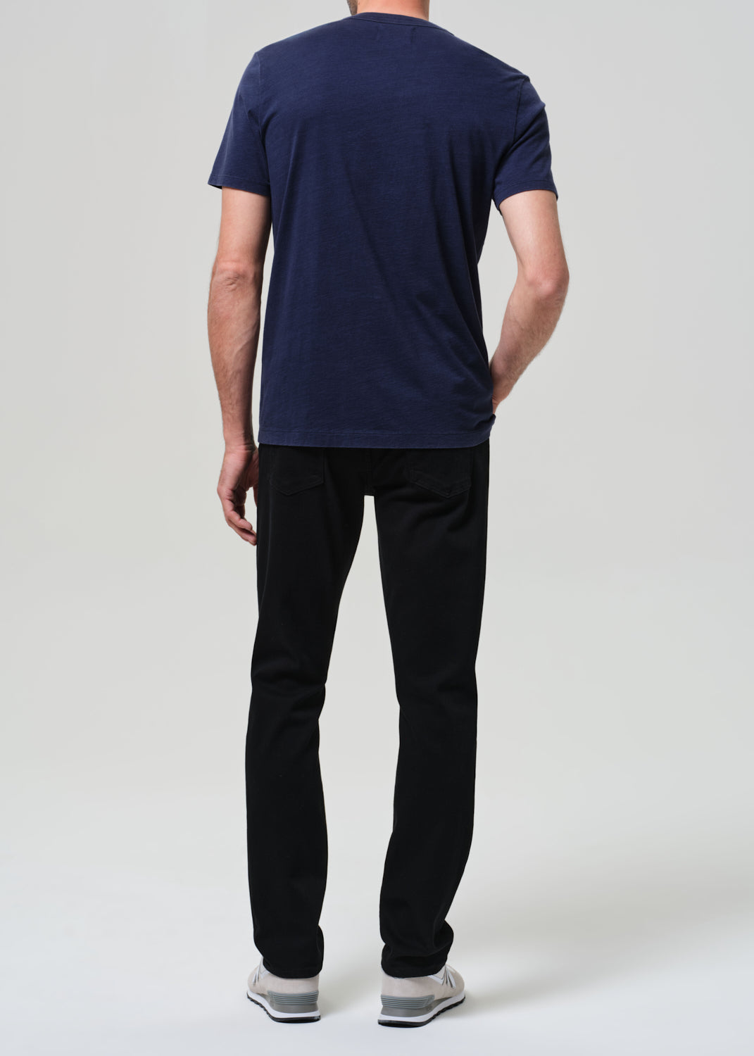 Person wearing a navy blue t-shirt and black jeans on a grey background