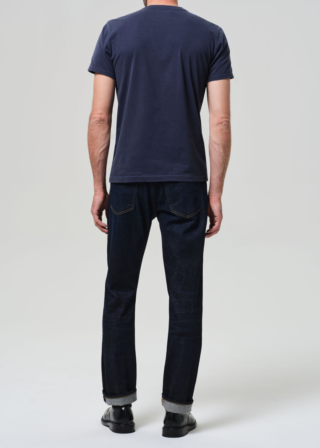 Person wearing a navy t-shirt and dark jeans on a white background