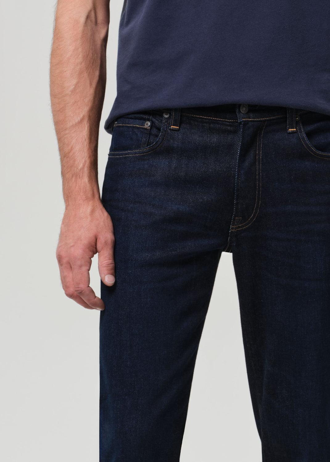 Person wearing dark blue jeans and a matching shirt on a light gray background