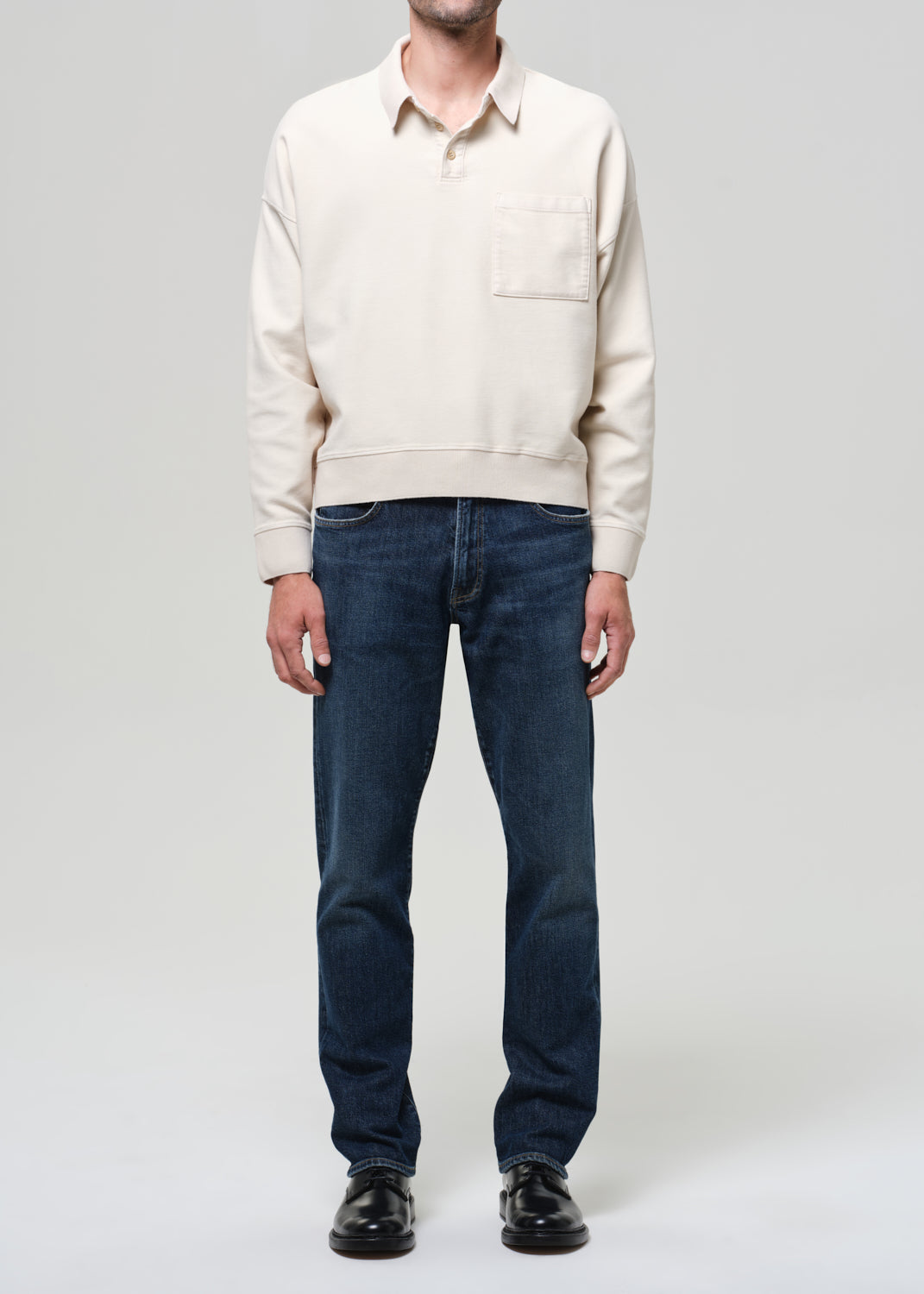 Person wearing a beige sweater and dark blue jeans on a plain background