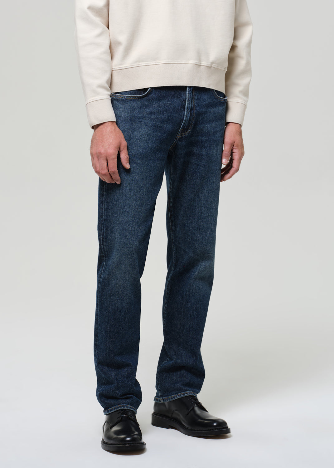 Person wearing blue jeans and a beige sweatshirt on a white background