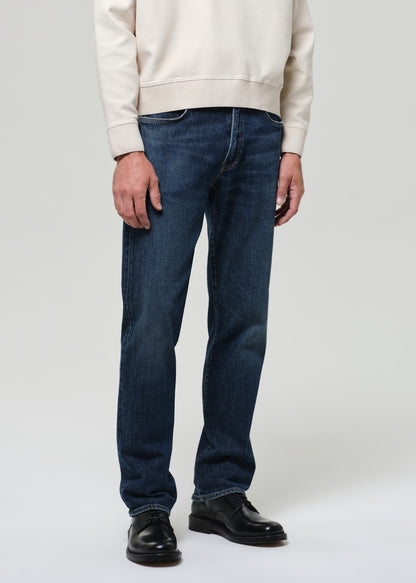 Person wearing blue jeans and a beige sweatshirt on a white background