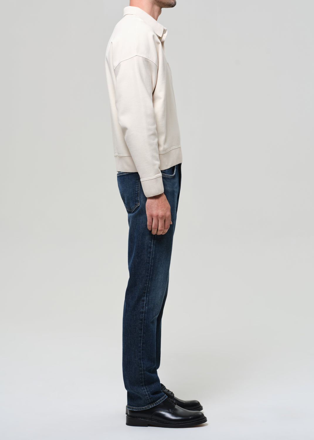 Person wearing a cream sweater and dark jeans on a white background