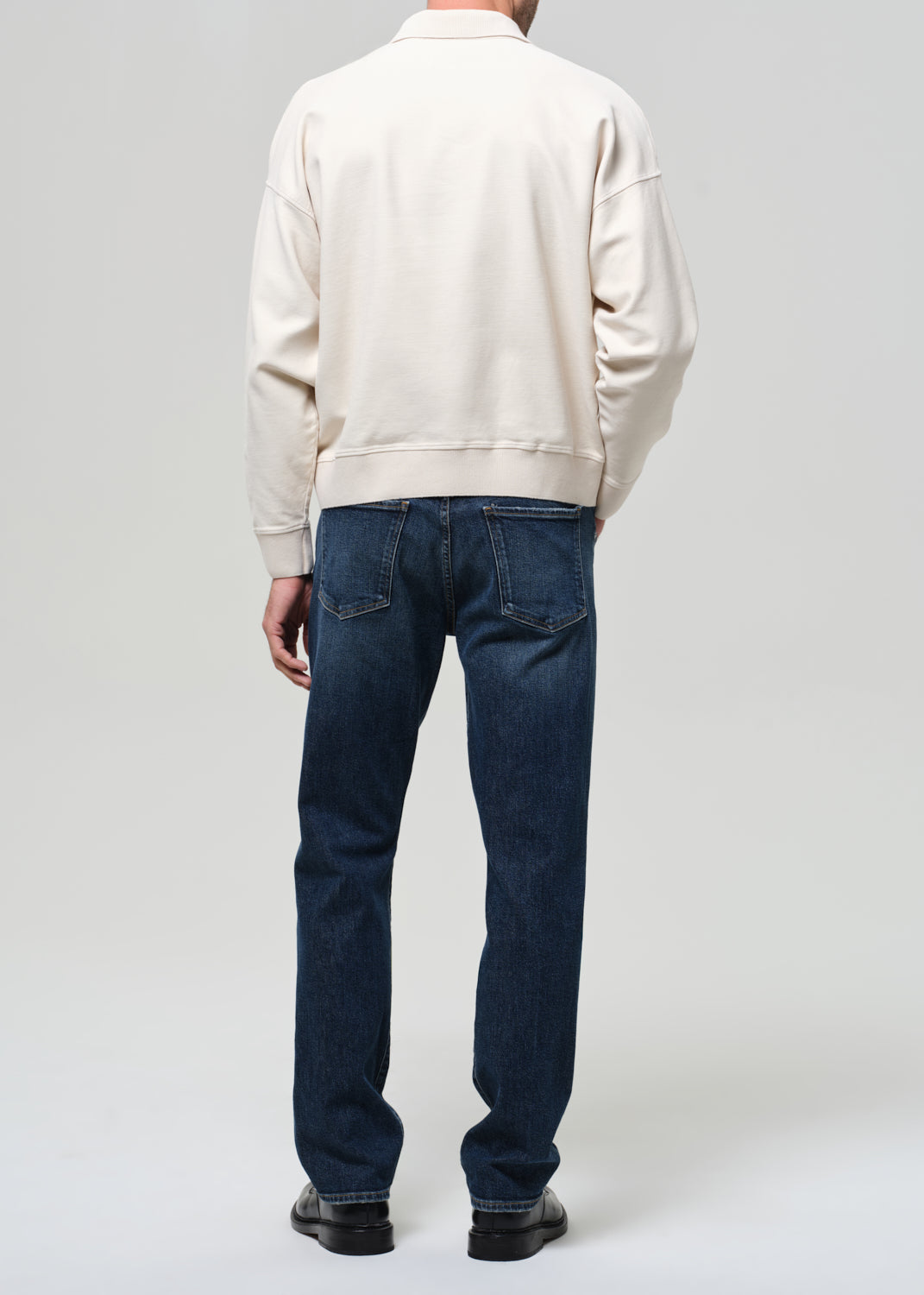 Person wearing a beige jacket and blue jeans on a white background