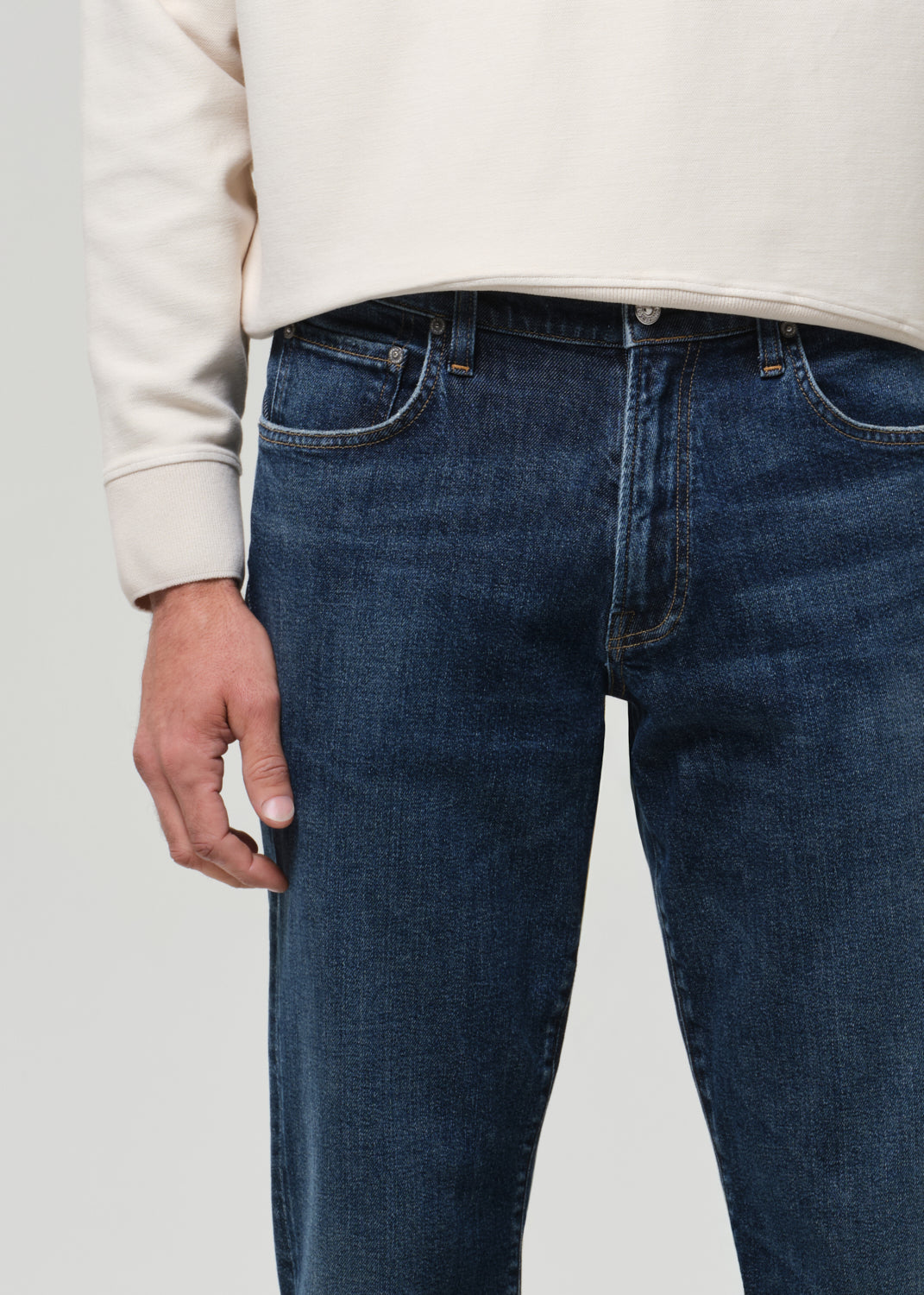 Person wearing blue jeans and a beige sweater on a plain background