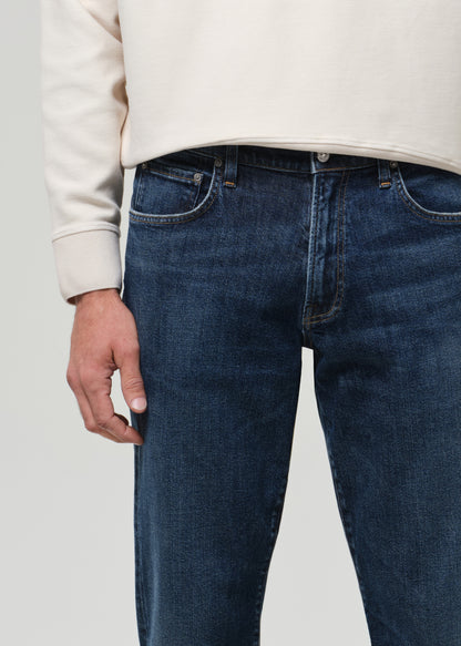 Person wearing blue jeans and a beige sweater on a plain background