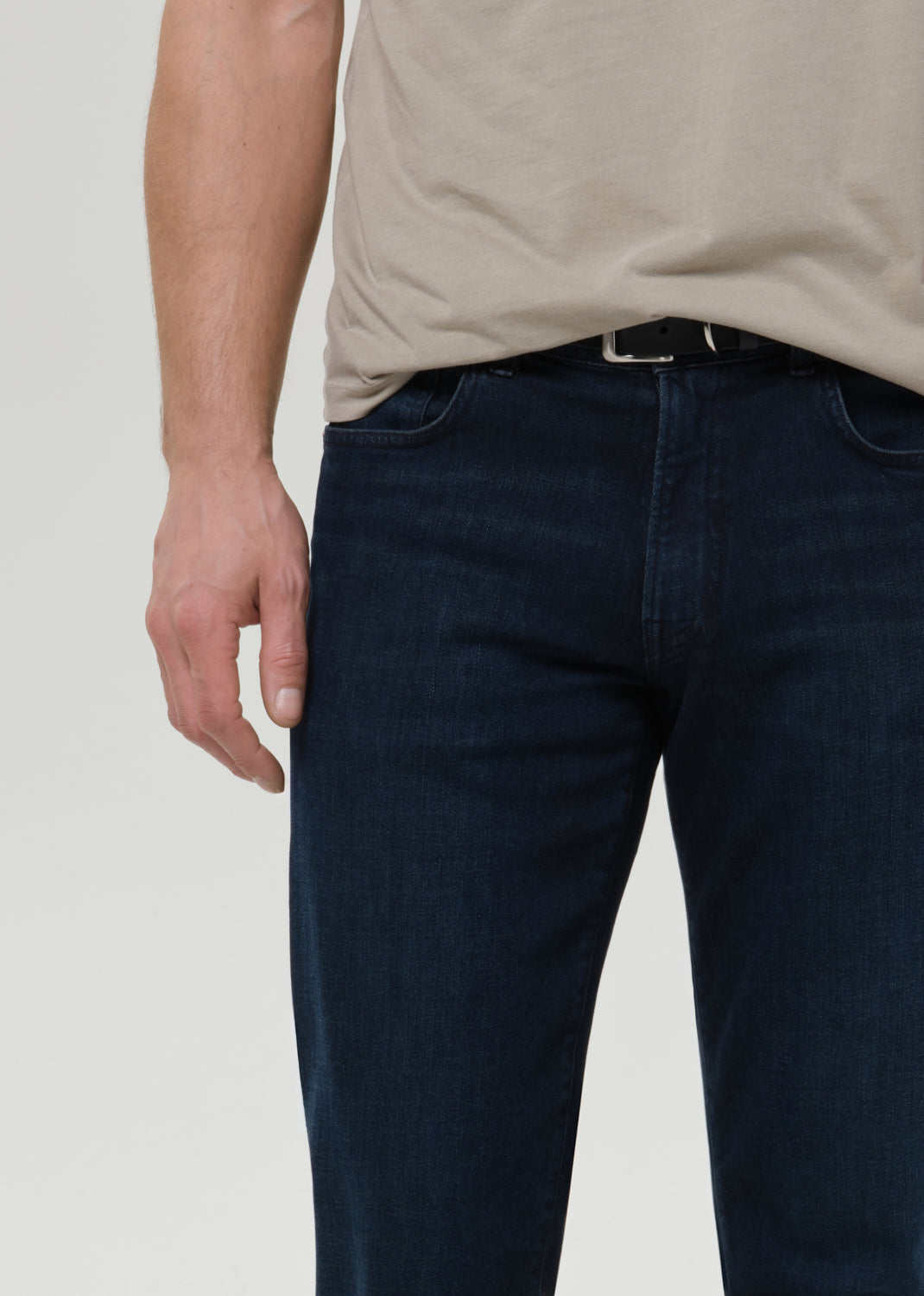 Person wearing dark blue jeans and a beige shirt on a plain background