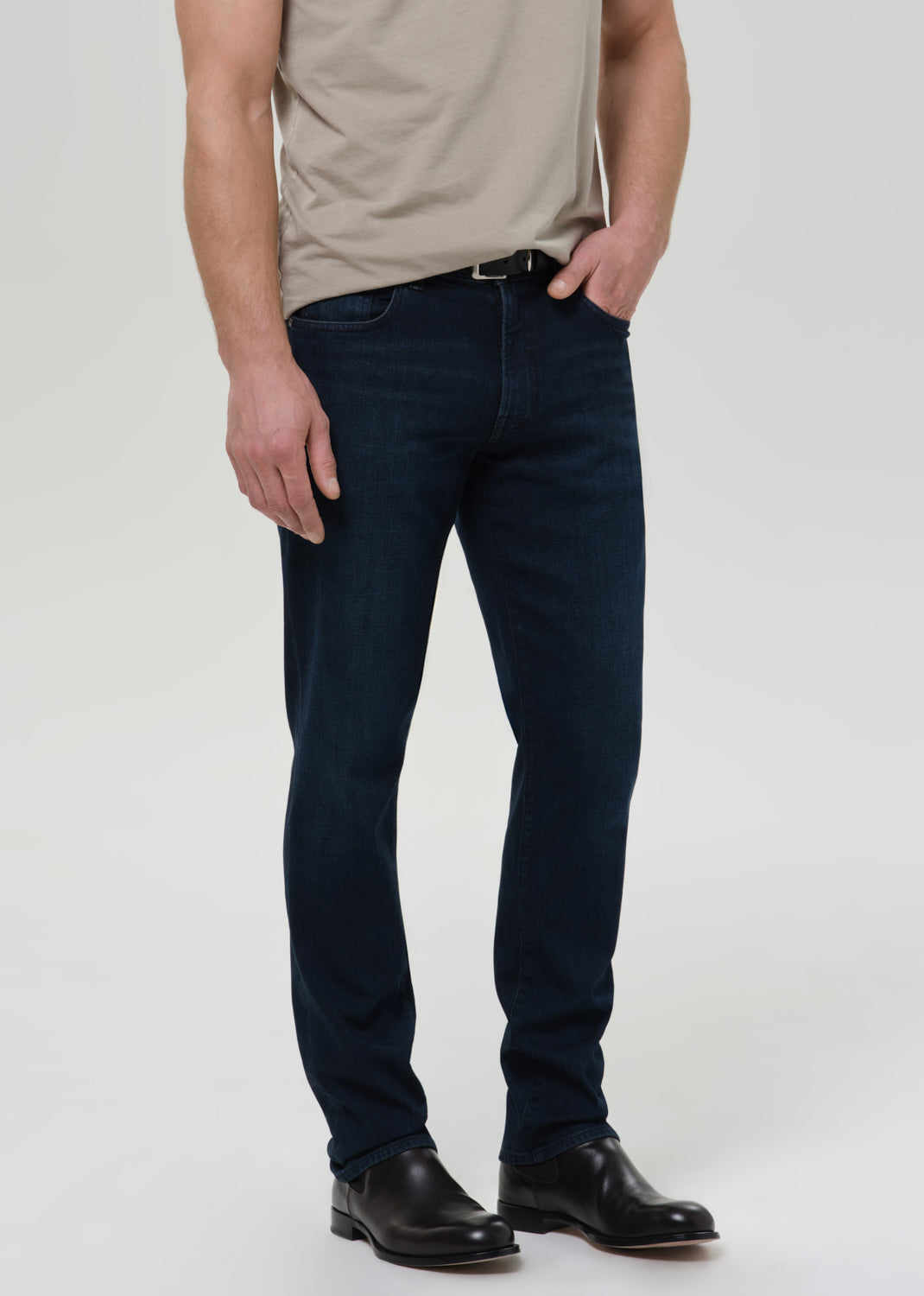Person wearing dark blue jeans and a beige shirt on a plain background