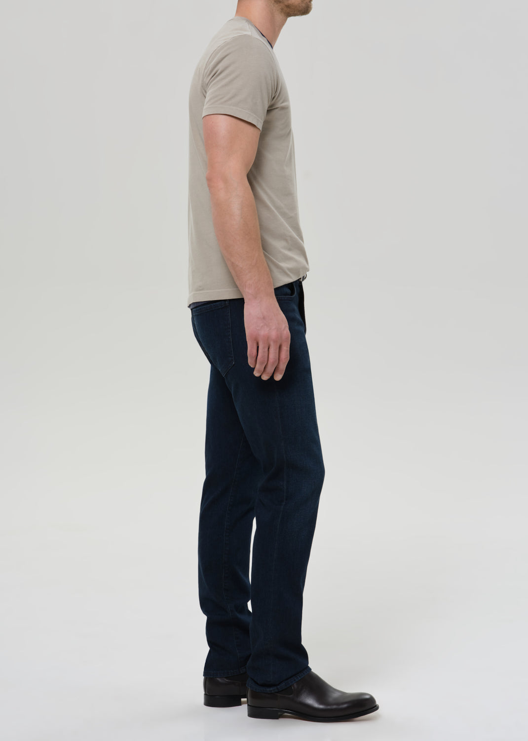 Man wearing a beige t-shirt and dark pants on a white background