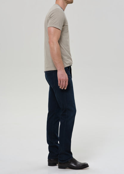 Man wearing a beige t-shirt and dark pants on a white background