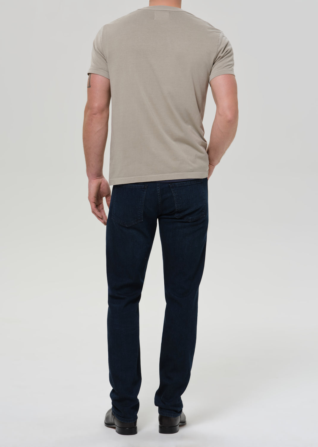 Person wearing a beige t-shirt and dark blue jeans on a white background