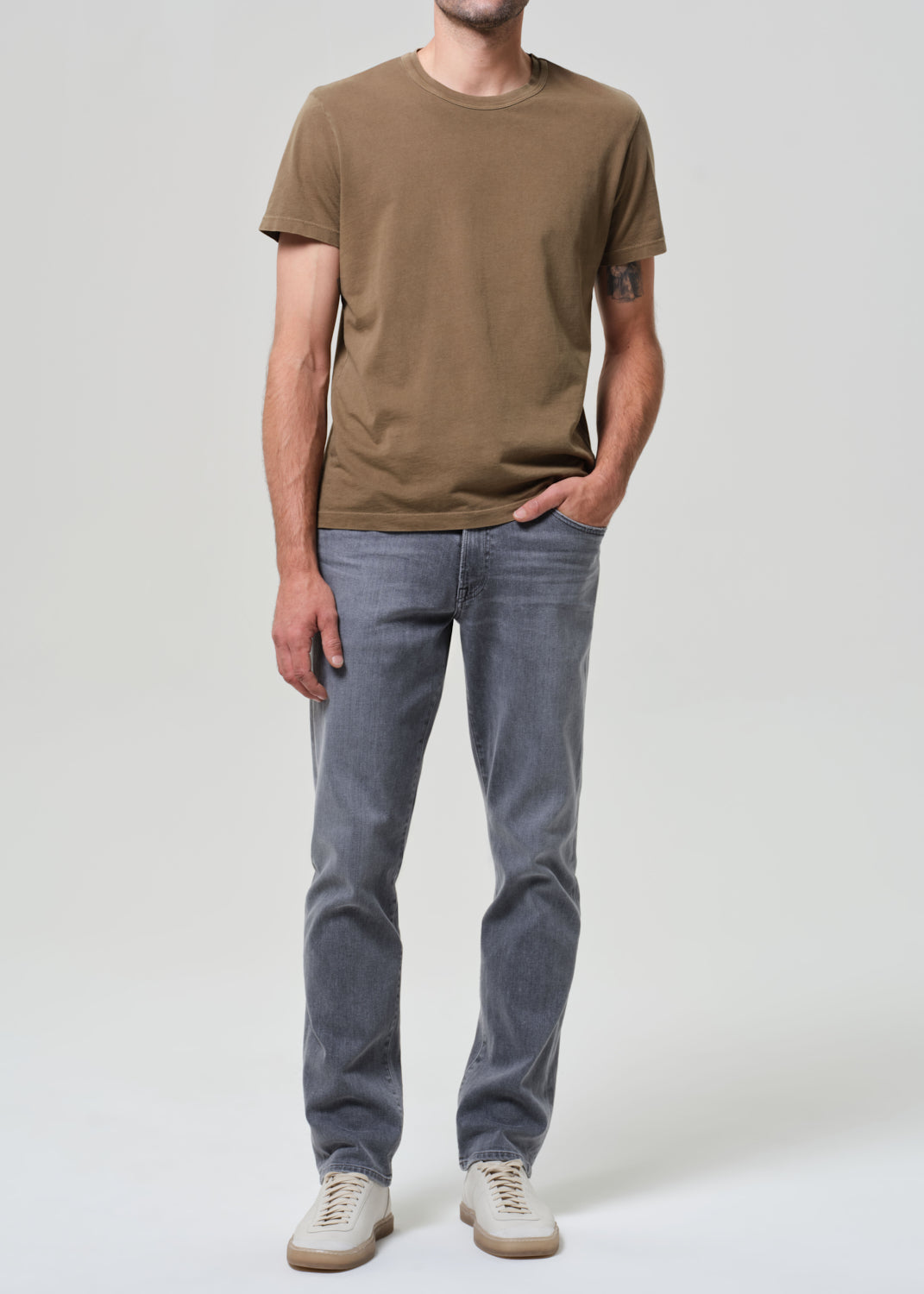 Person wearing a brown t-shirt and gray jeans on a grey background