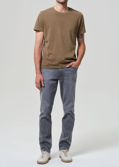 Person wearing a brown t-shirt and gray jeans on a grey background