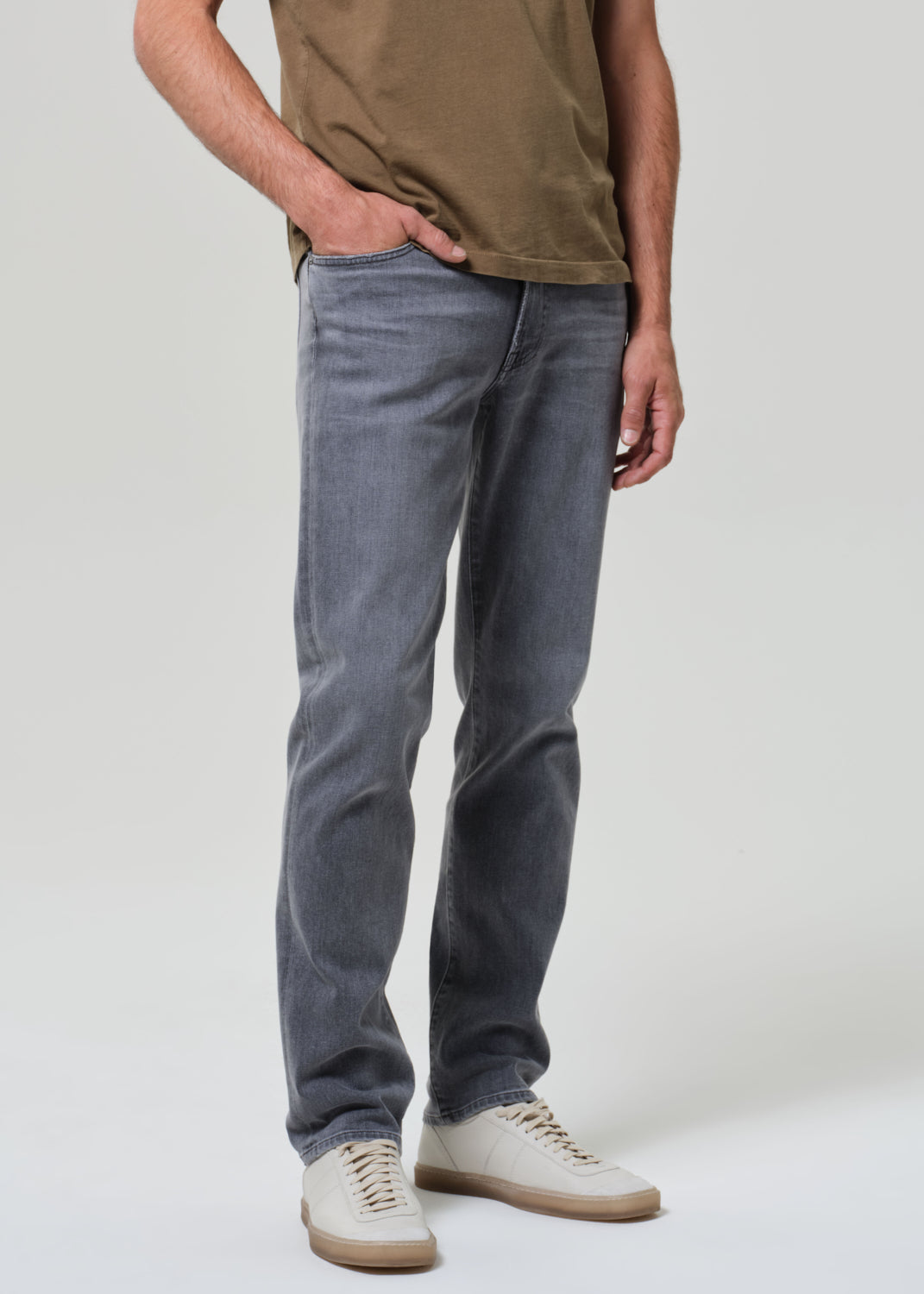 Person wearing a brown t-shirt and gray jeans on a grey background
