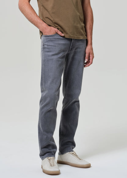Person wearing a brown t-shirt and gray jeans on a grey background