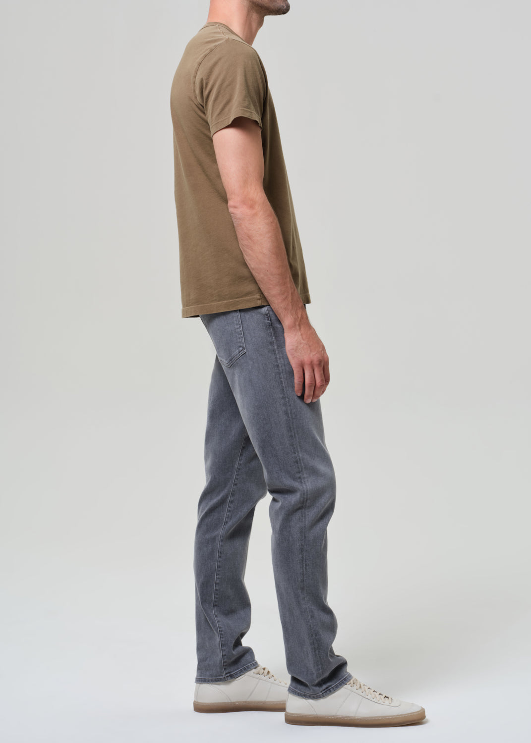 Person wearing a brown t-shirt and gray jeans on a grey background