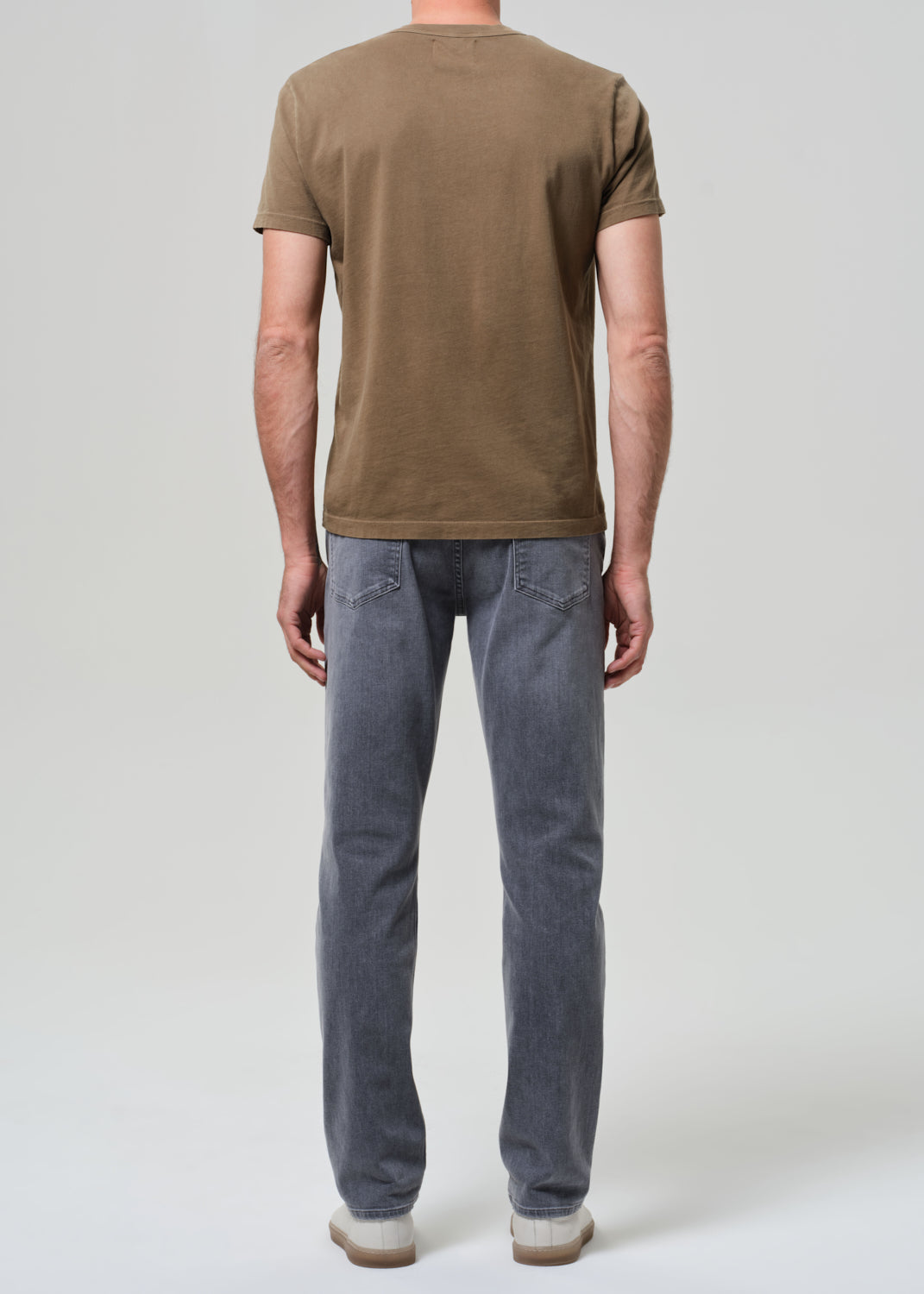 Person wearing a brown t-shirt and gray jeans on a grey background