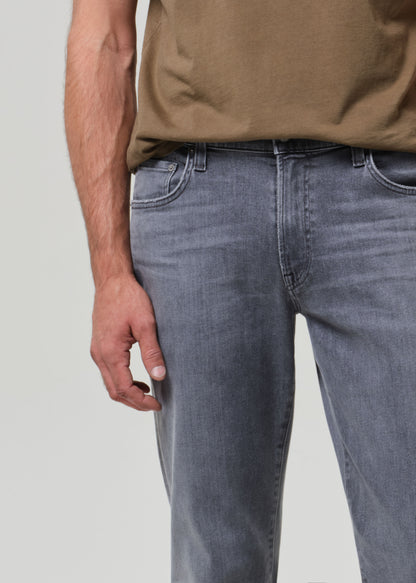 Person wearing a brown t-shirt and gray jeans on a grey background