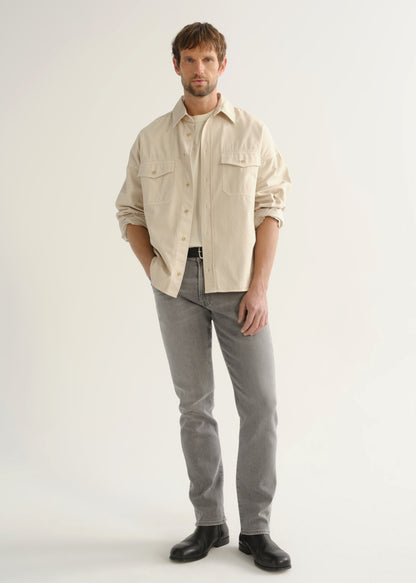 Person wearing a cream button-front shirt, grey jeans, and black boots, front full body view on a light grey background.