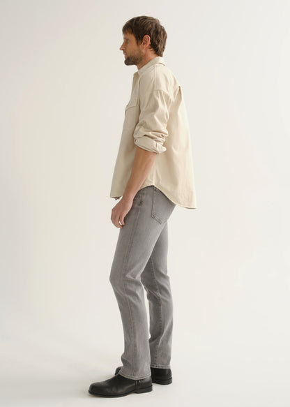 Person wearing a cream button-front shirt, grey jeans, and black boots, side full body view on a light grey background.