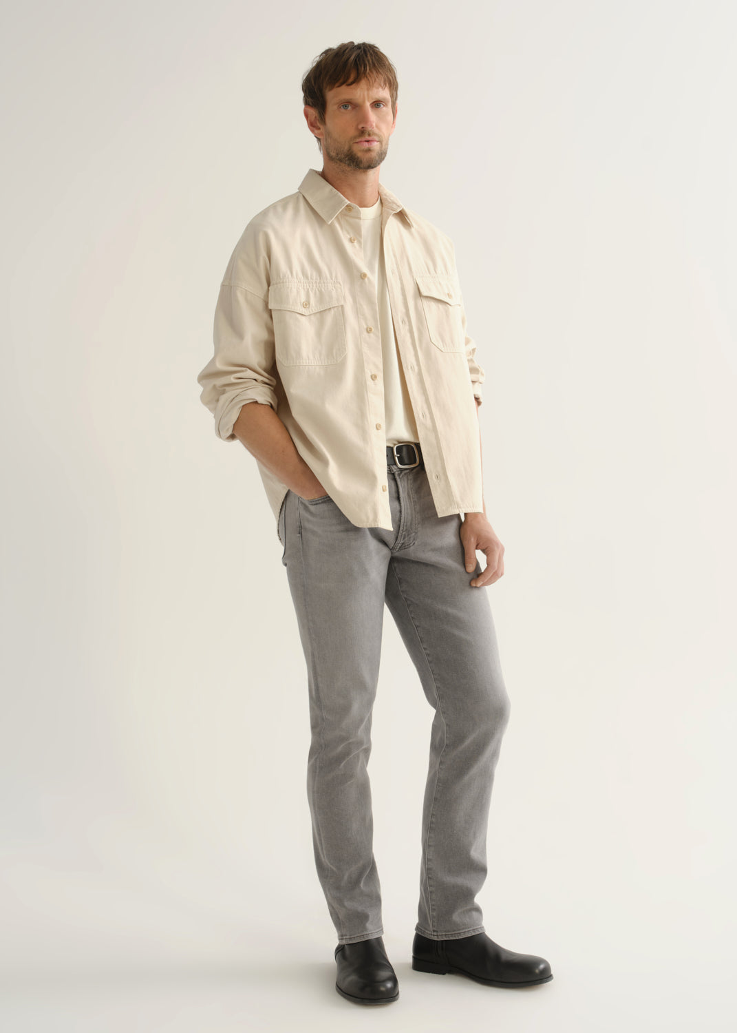 Person wearing a cream button-front shirt, grey jeans, and black boots, angled front full body view on a light grey background.