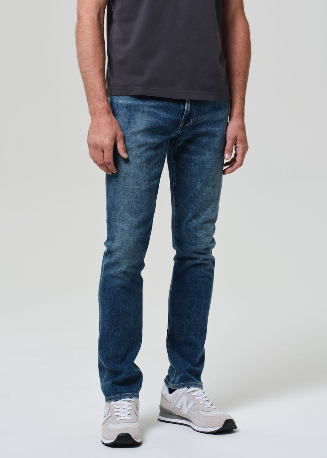 Person wearing blue jeans and white sneakers on a plain background