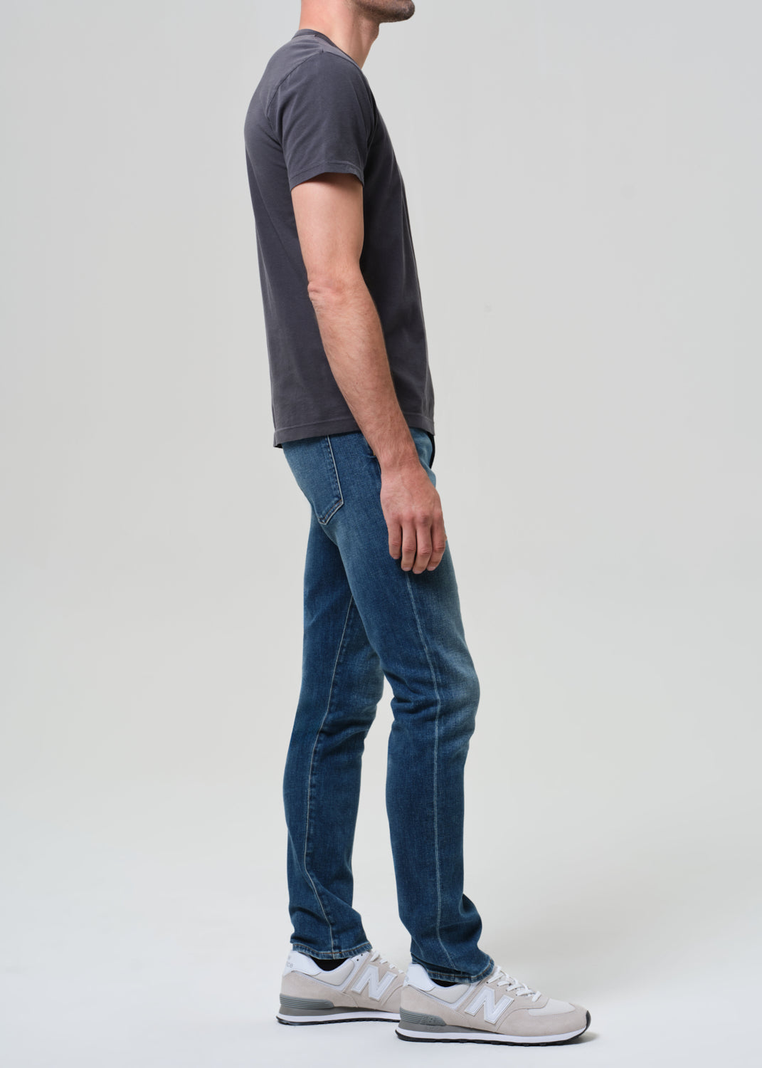 Person wearing a dark gray t-shirt and blue jeans standing against a plain background