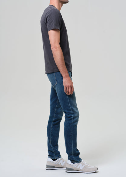 Person wearing a dark gray t-shirt and blue jeans standing against a plain background